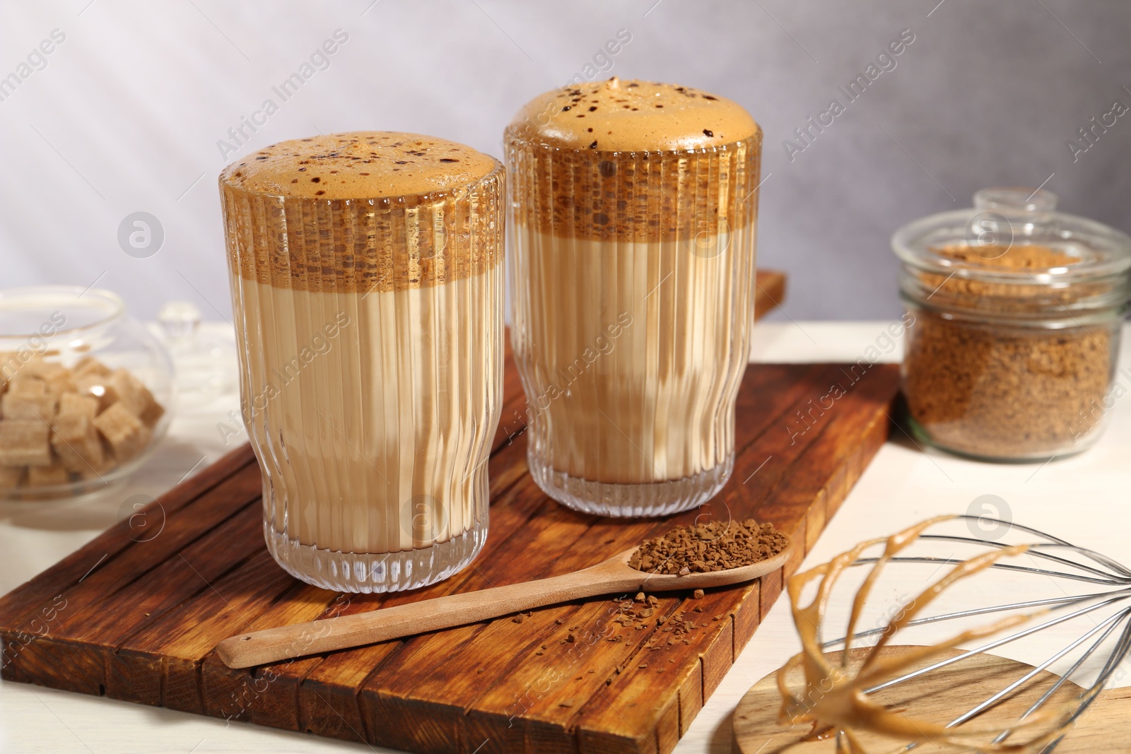 Delicious dalgona coffee in glasses, whisk, brown sugar and granules on light table, closeup Photo of Delicious dalgona coffee in glasses, whisk, brown sugar and granules on light table, closeup
