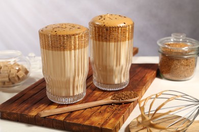 Photo of Delicious dalgona coffee in glasses, whisk, brown sugar and granules on light table, closeup