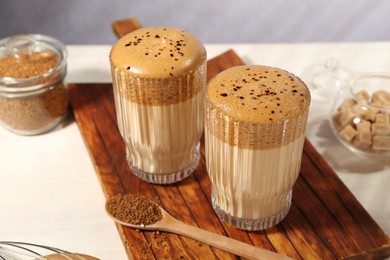 Photo of Delicious dalgona coffee in glasses, brown sugar and granules on light table, closeup