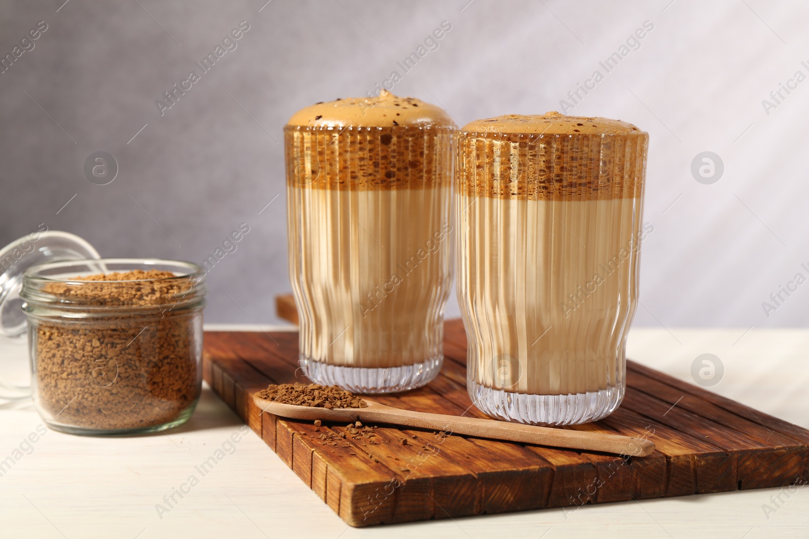 Photo of Delicious dalgona coffee in glasses and granules on light table, closeup