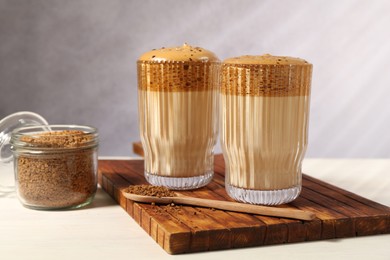 Photo of Delicious dalgona coffee in glasses and granules on light table, closeup