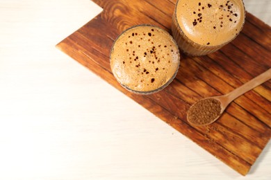 Photo of Delicious dalgona coffee in glasses and granules on light table, top view. Space for text