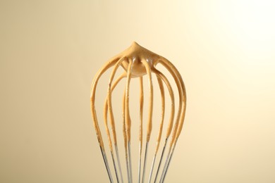 Photo of Making delicious dalgona coffee. Whisk with cream on beige background, closeup