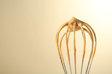 Photo of Making delicious dalgona coffee. Whisk with cream on beige background, closeup. Space for text