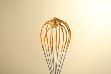 Photo of Making delicious dalgona coffee. Whisk with cream on beige background, closeup