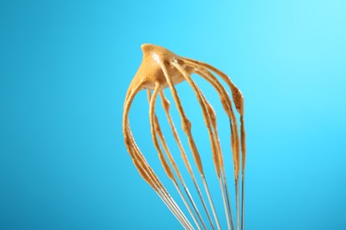 Photo of Making delicious dalgona coffee. Whisk with cream on light blue background, closeup