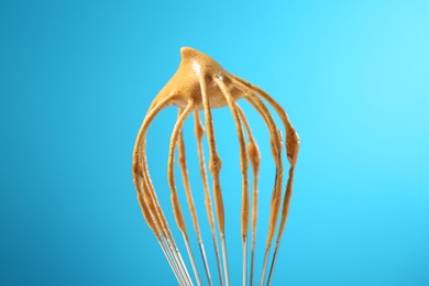 Photo of Making delicious dalgona coffee. Whisk with cream on light blue background, closeup