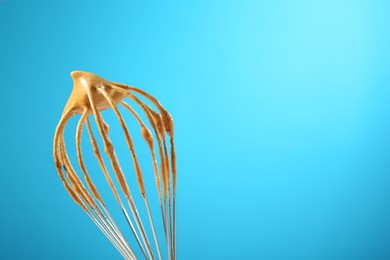 Photo of Making delicious dalgona coffee. Whisk with cream on light blue background, closeup. Space for text