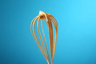 Photo of Making delicious dalgona coffee. Whisk with cream on light blue background, closeup