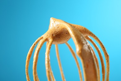 Photo of Making delicious dalgona coffee. Whisk with cream on light blue background, closeup