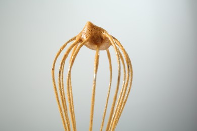 Photo of Making delicious dalgona coffee. Whisk with cream on light grey background, closeup