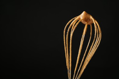 Photo of Making delicious dalgona coffee. Whisk with cream on black background, closeup. Space for text