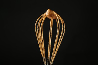 Photo of Making delicious dalgona coffee. Whisk with cream on black background, closeup