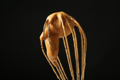 Photo of Making delicious dalgona coffee. Whisk with cream on black background, closeup