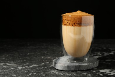 Photo of Delicious dalgona coffee in glass on dark marble table, space for text