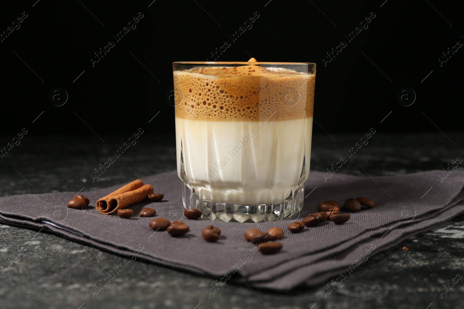Photo of Delicious dalgona coffee in glass, beans and cinnamon on dark marble table, closeup