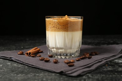 Photo of Delicious dalgona coffee in glass, beans and cinnamon on dark marble table, closeup