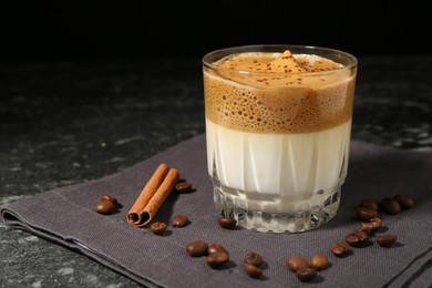 Photo of Delicious dalgona coffee in glass, beans and cinnamon on dark marble table, closeup. Space for text