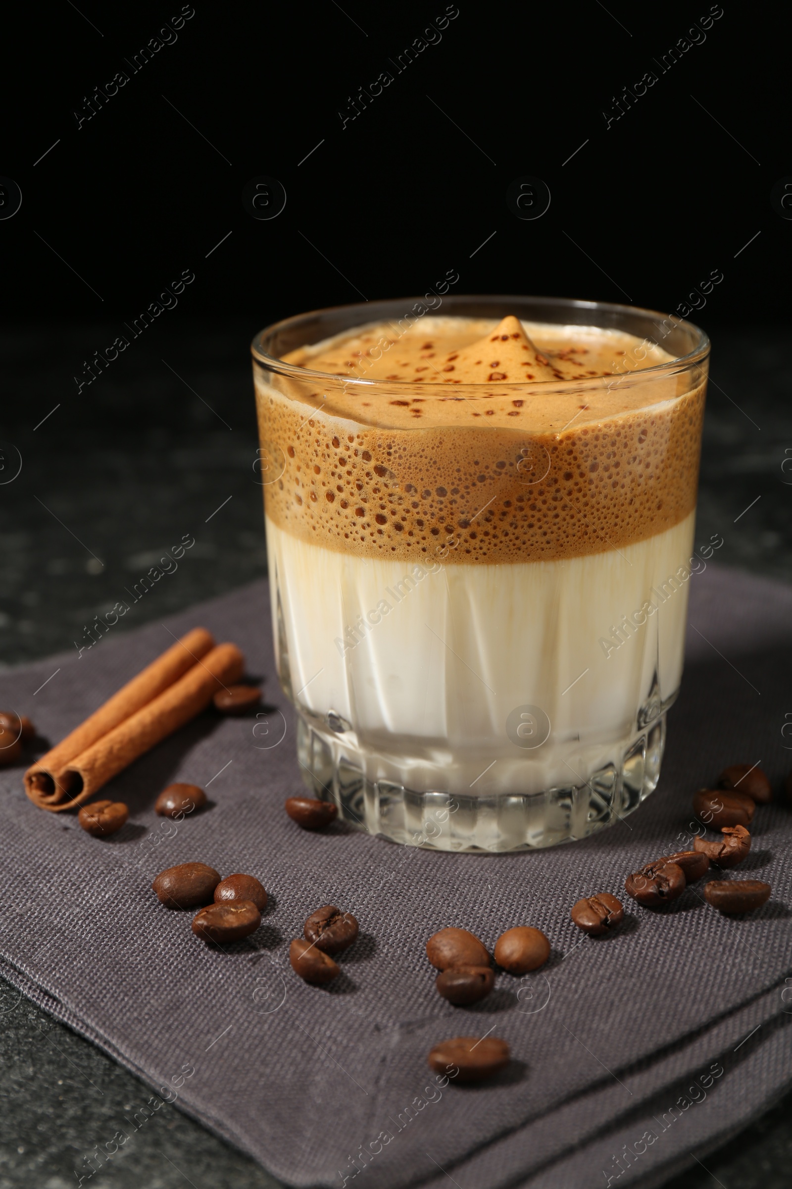 Photo of Delicious dalgona coffee in glass, beans and cinnamon on dark table, closeup
