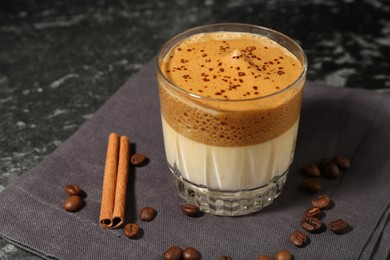 Photo of Delicious dalgona coffee in glass, beans and cinnamon on dark marble table, closeup