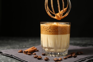 Photo of Pouring cream for dalgona coffee into glass at dark table, closeup. Space for text