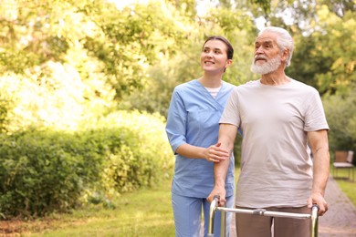 Photo of Smiling nurse with elderly man who using walking frame outdoors. Space for text