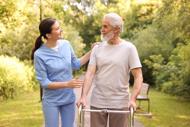 Photo of Smiling nurse supporting elderly man who using walking frame outdoors