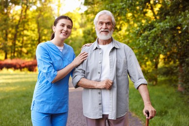 Photo of Smiling nurse supporting elderly man with walking cane outdoors
