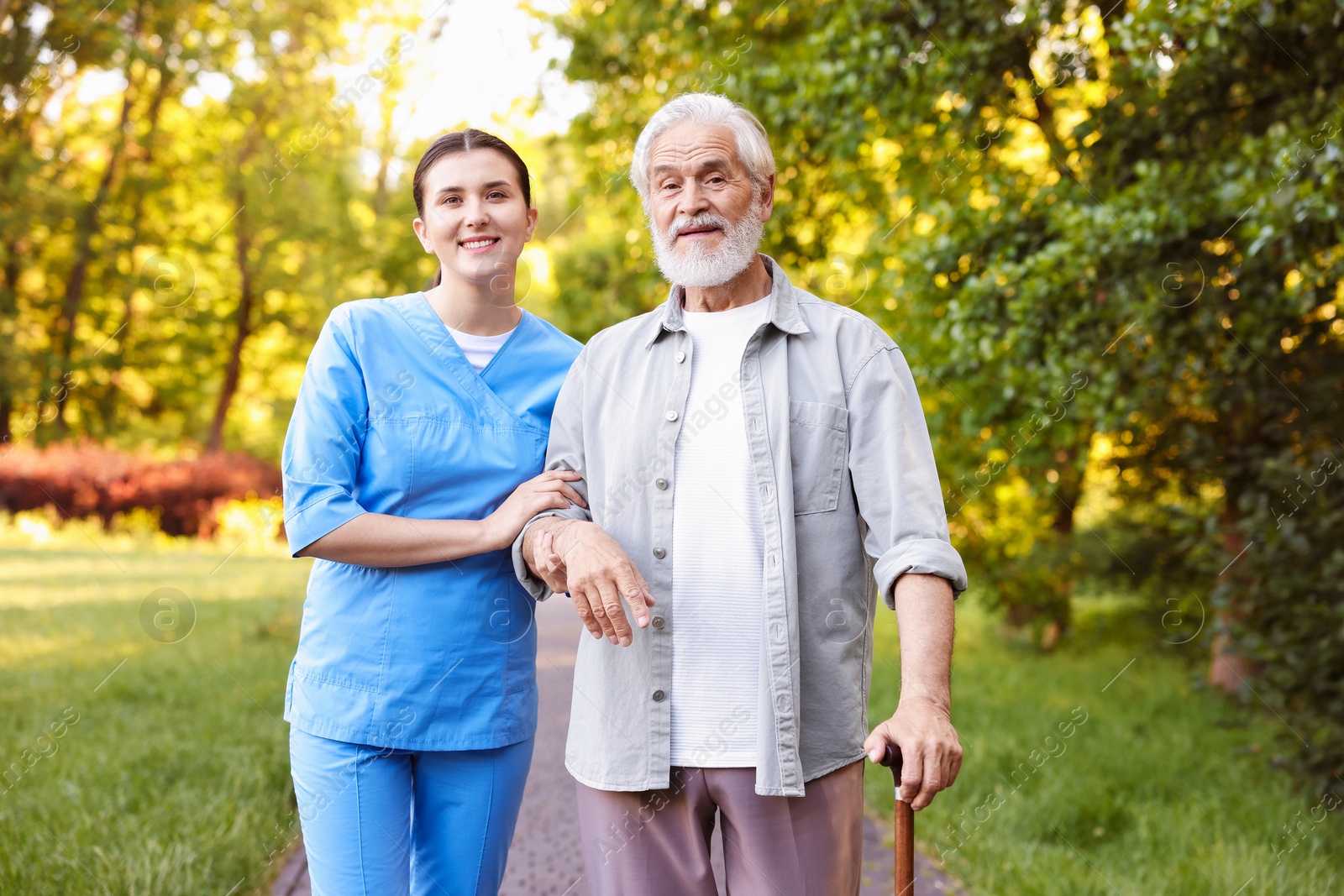 Smiling nurse supporting elderly man with walking cane outdoors Photo of Smiling nurse supporting elderly man with walking cane outdoors