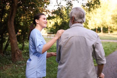 Photo of Smiling nurse supporting elderly man in park