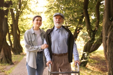 Photo of Smiling caregiver supporting elderly man who using walking frame outdoors