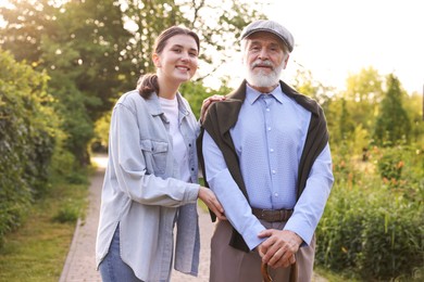 Photo of Portrait of smiling caregiver and elderly man with walking cane outdoors
