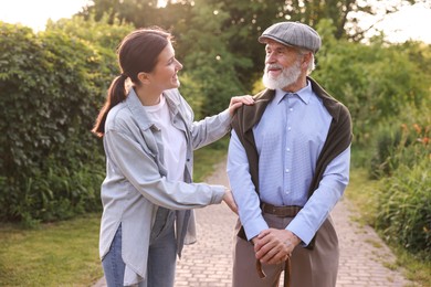 Photo of Smiling caregiver supporting elderly man with walking cane outdoors