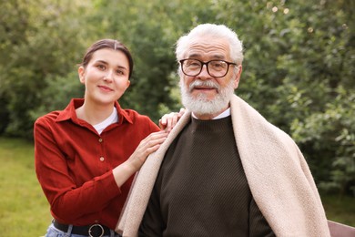 Photo of Portrait of smiling caregiver and elderly man in glasses outdoors
