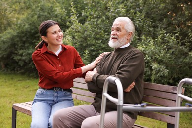 Photo of Smiling caregiver supporting elderly man with walking frame outdoors