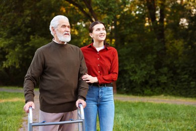 Photo of Smiling caregiver supporting elderly man who using walking frame outdoors