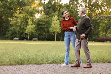 Photo of Smiling caregiver supporting elderly man who using walking cane outdoors. Space for text