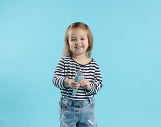 Photo of Cute little girl with microphone on light blue background
