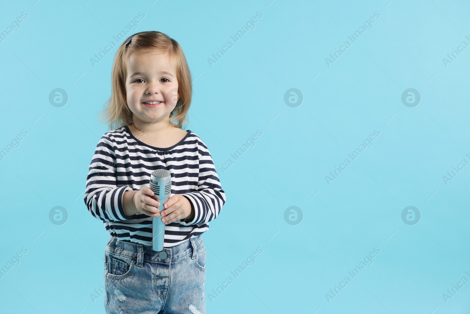 Photo of Cute little girl with microphone on light blue background, space for text