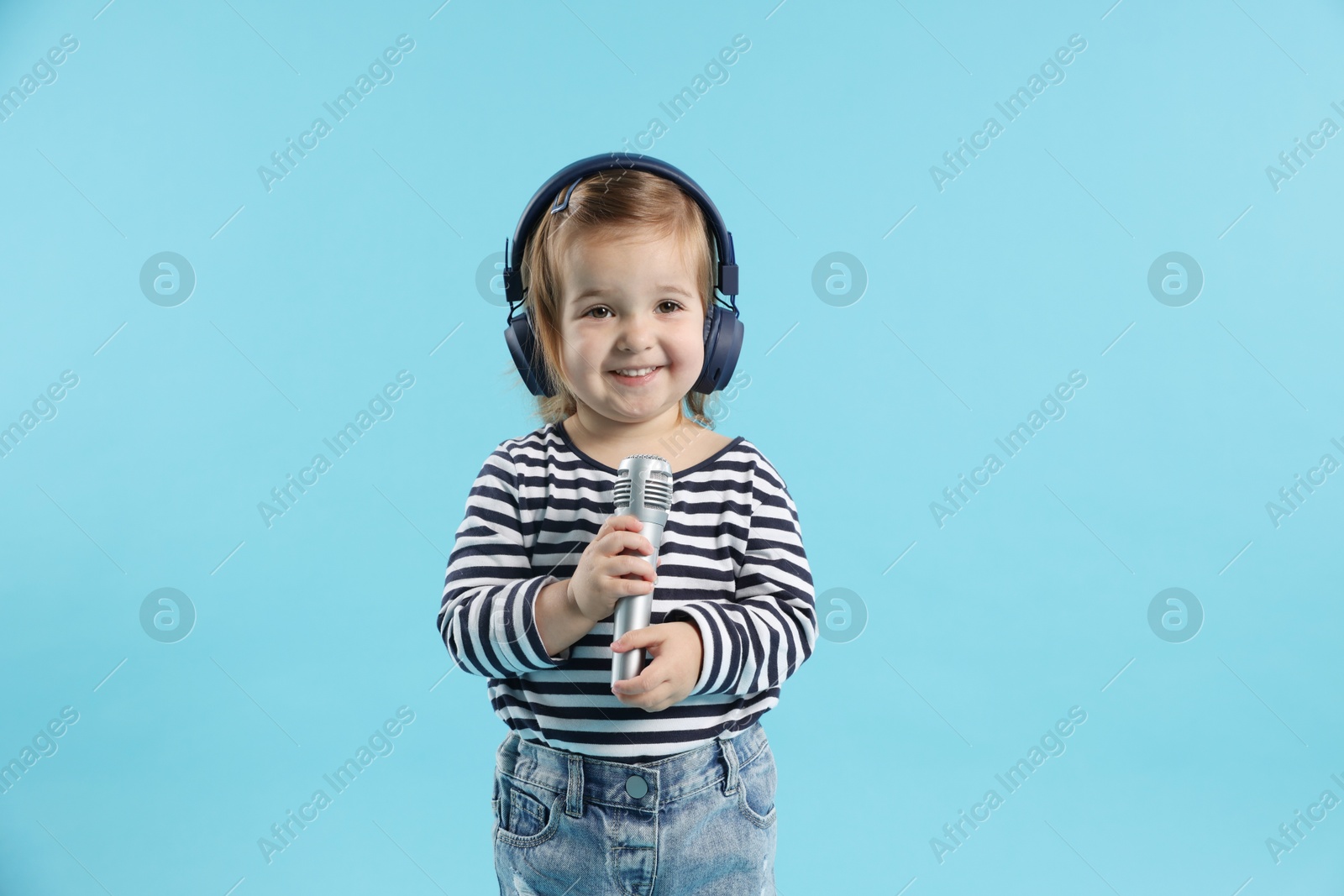 Cute little girl with headphones and microphone on light blue background Photo of Cute little girl with headphones and microphone on light blue background