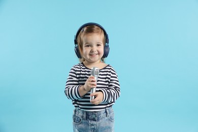 Photo of Cute little girl with headphones and microphone on light blue background