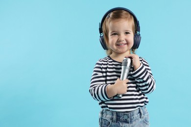 Photo of Cute little girl with headphones and microphone on light blue background, space for text