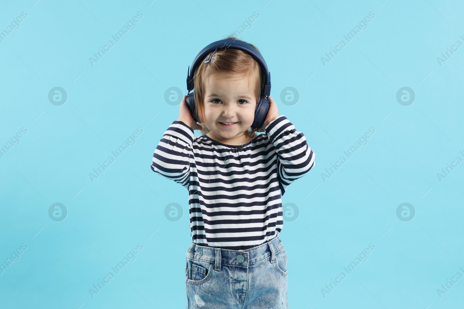 Photo of Cute little girl in headphones on light blue background