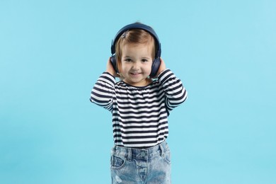 Photo of Cute little girl in headphones on light blue background