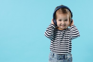 Photo of Cute little girl in headphones on light blue background, space for text
