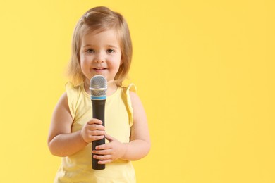 Photo of Cute little girl with microphone on yellow background, space for text