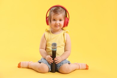 Photo of Cute little girl with headphones and microphone on yellow background