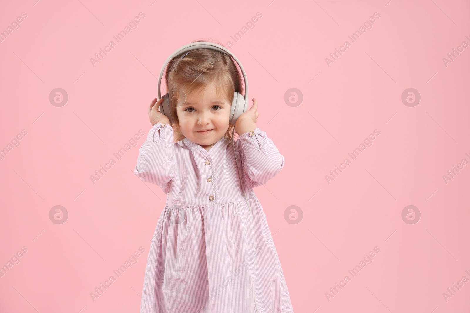Cute little girl in headphones on pink background Photo of Cute little girl in headphones on pink background
