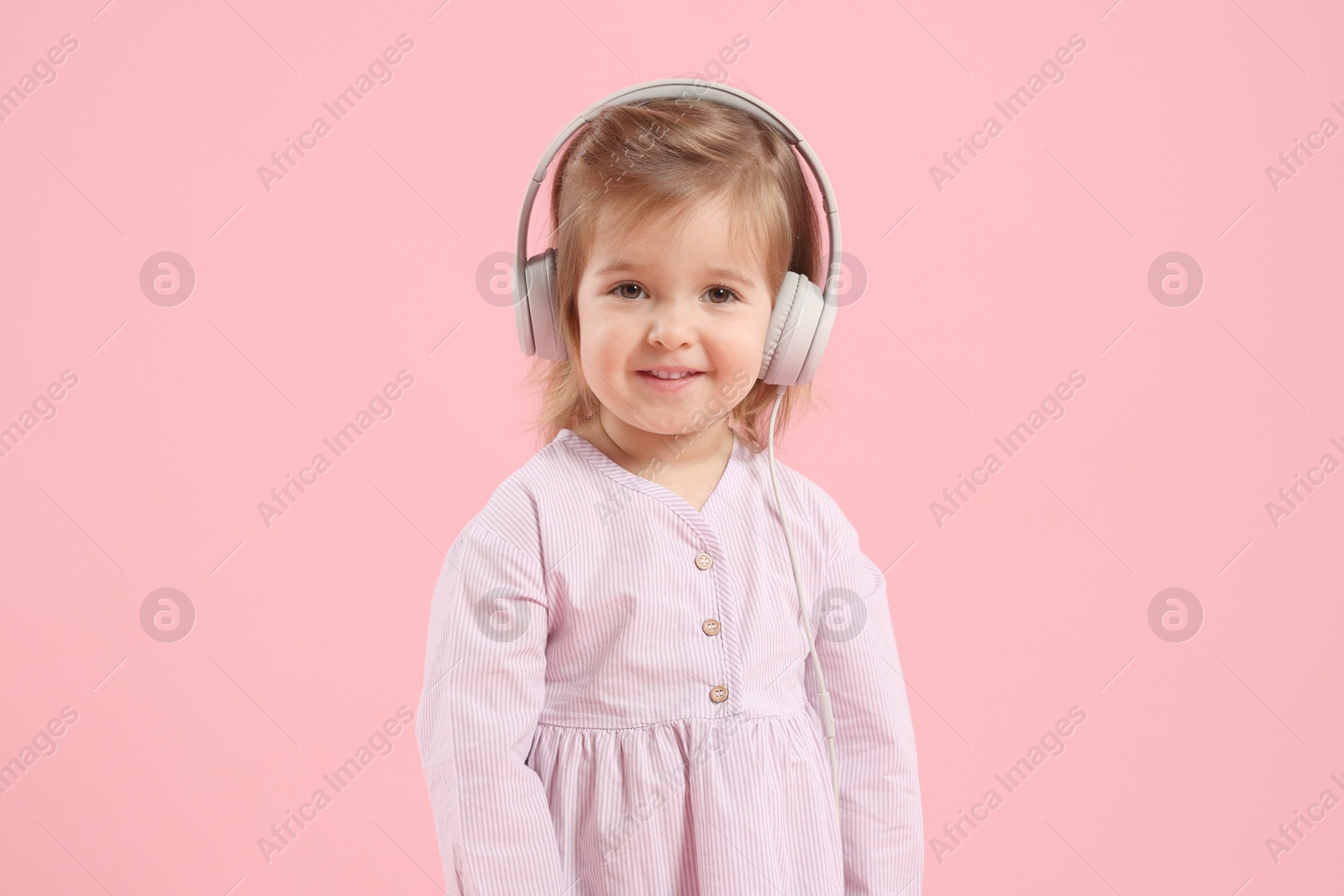 Cute little girl in headphones on pink background Photo of Cute little girl in headphones on pink background