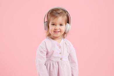 Photo of Cute little girl in headphones on pink background